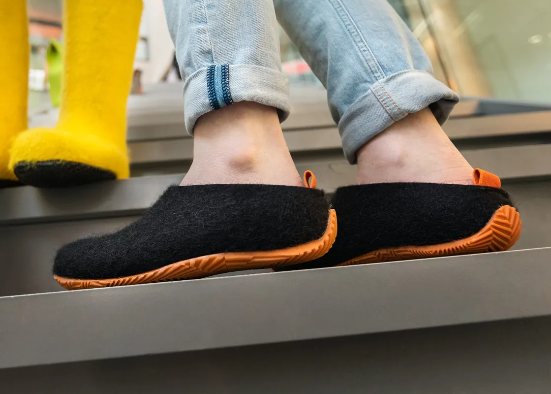 Black wool-felt shoes with orange sole and heel loop, worn on stairs with jeans.